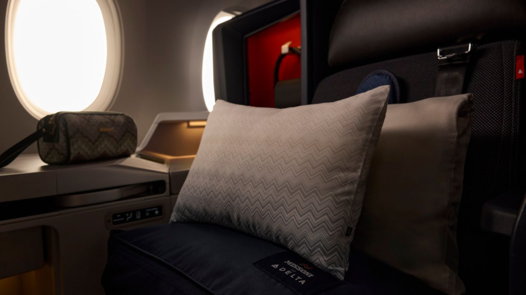 Airplane seat in business class featuring a patterned pillow and a matching amenity kit.