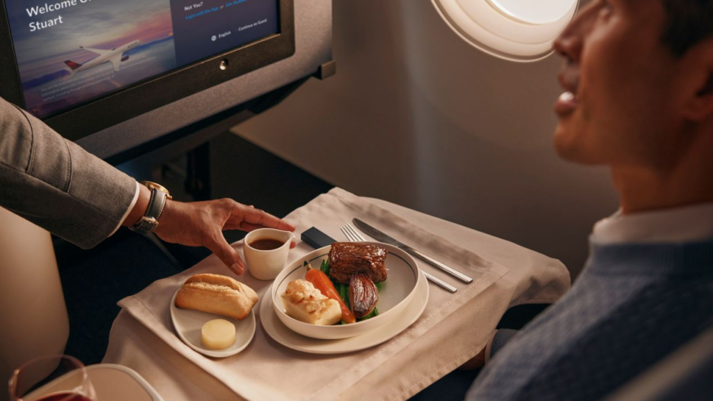 A flight attendant placing a small pitcher on an airline meal tray in front of a passenger.