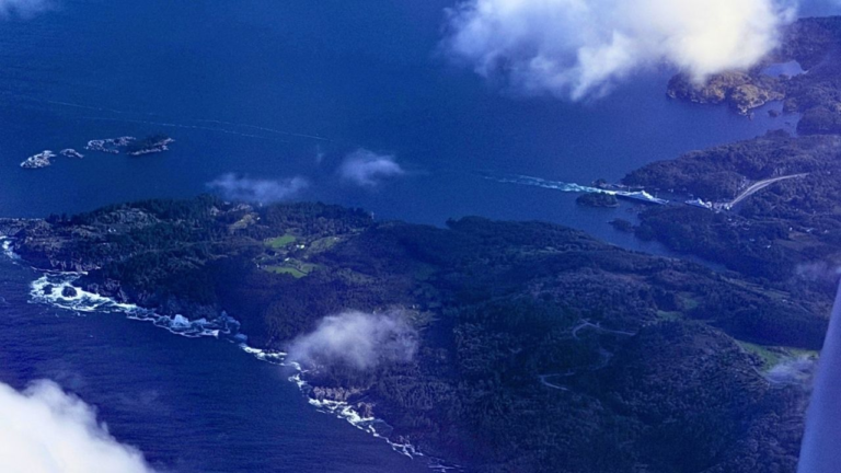 Aerial view of a coastal landscape with forested islands and dark blue water, ideal for Europe travel, showing a ferry leaving a wake near a dock.