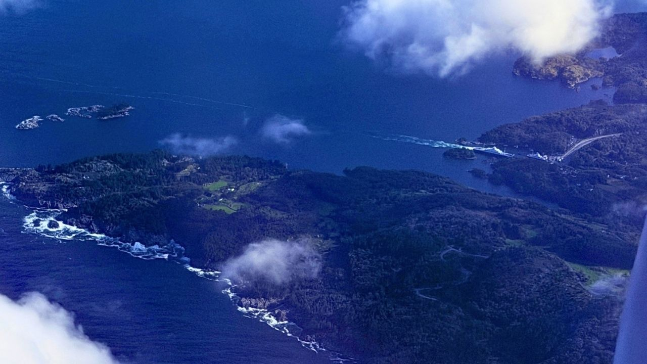 Aerial view of a coastal landscape with forested islands and dark blue water, ideal for Europe travel, showing a ferry leaving a wake near a dock.