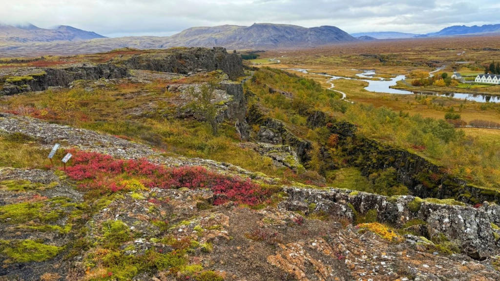 A deep canyon with mossy rock walls running through a grassy Icelandic landscape with a winding river and distant mountains.